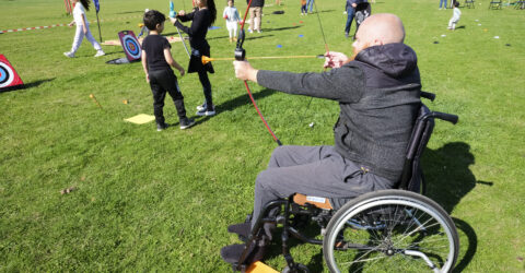 Photo d'une personne en fauteuil roulant participant à une animation de tir à l'arc en plein air.