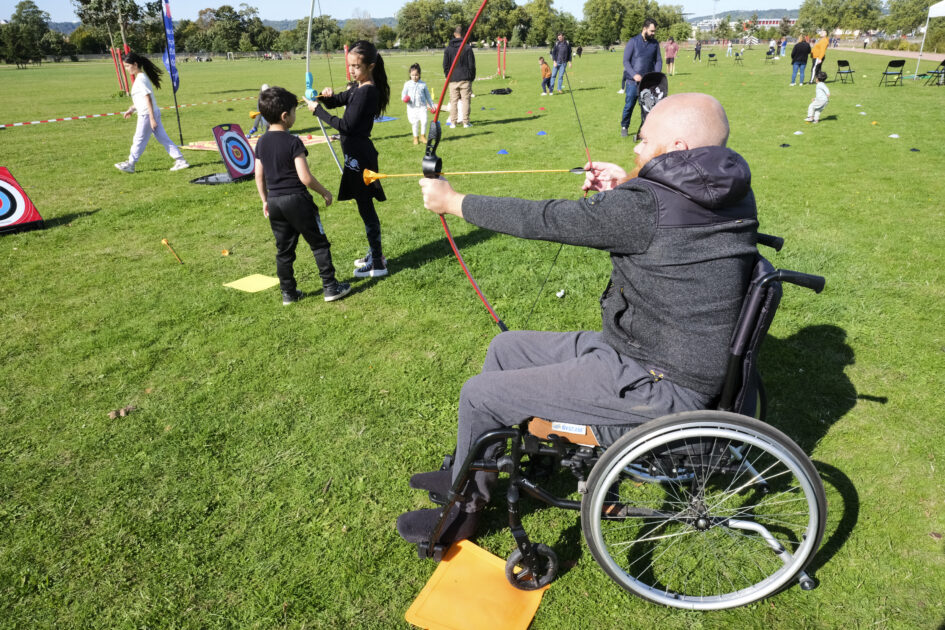 Photo d'une personne en fauteuil roulant participant à une animation de tir à l'arc en plein air.